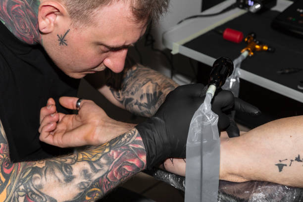 istock Master bends over man's arm and makes tattoo on it 1162623159