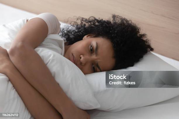 Sad Depressed African Woman Hugging Pillow Lying In Bed Alone Stock Photo - Download Image Now