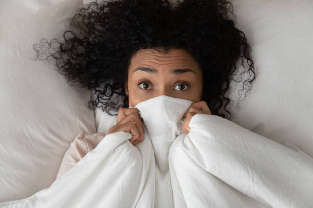 Surprised funny african girl in bed covering face with blanket Surprised scared funny african girl lying in bed covering face with blanket, young black woman awake from sleep hiding peeking from duvet feel shy afraid or bad dream nightmare embarrassed, top view camera covers pictures stock pictures, royalty-free photos & images