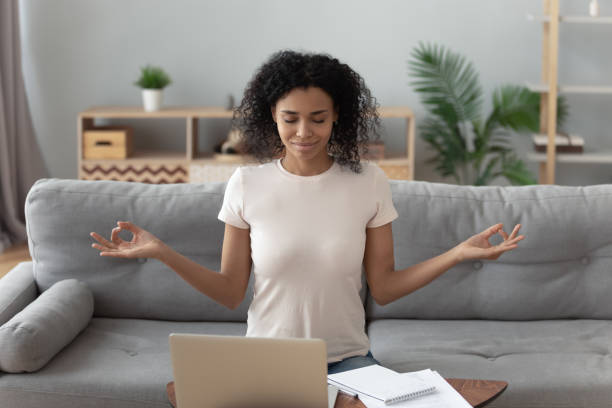 Serene african girl sit on couch meditating feel no stress Serene happy calm african girl student sit on couch take break from computer work study do yoga exercise breath fresh air at home, mindful healthy woman relax meditating feel no stress free concept meditation room office stock pictures, royalty-free photos & images