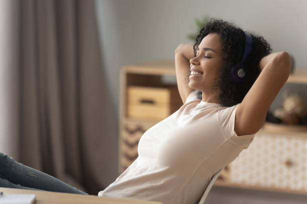 Happy african girl wearing headphones relaxing listening to music Happy african american girl wearing headphones relaxing listening to music taking break at work, calm smiling young black woman enjoying good lounge sound for stress relief sit at home office desk meditation room office stock pictures, royalty-free photos & images
