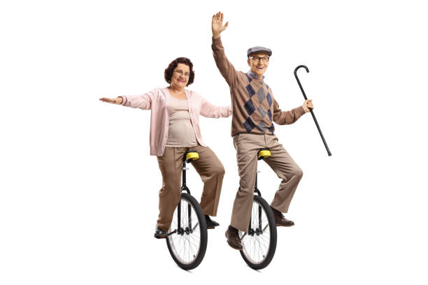 elderly man holding a walking cane and an elderly woman riding unicycles and smiling - unicycle unicycling cycling wheel imagens e fotografias de stock