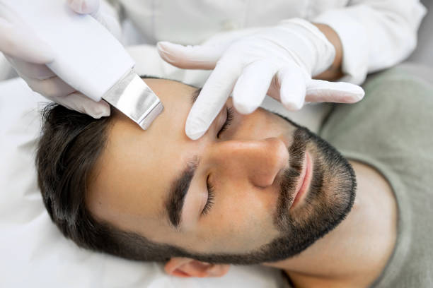 Young Man in Beauty Clinic Receiving Ultrasound Facial Cleaning Procedure - fotografia de stock