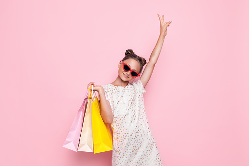 Happy girl in stylish dress, teenager with purchases in hand, after a shopping trip on a pink background