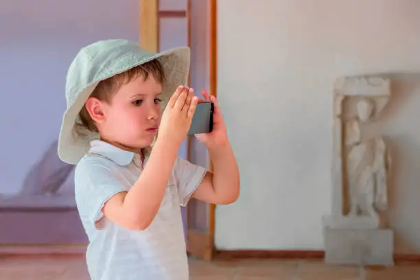 Little filmmaker. Taking a photo process. Kid at media school. Boy taking a picture of exhibit at art gallery, museum. Traveller background. Portrait of child with gadget. Showing interest to artefact