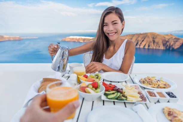 Couple Eating Breakfast On Terrace Resort Travel Couple eating breakfast. Smiling tourist woman drinking coffee and man drinking orange juice on terrace resort outdoor. Healthy and delicious food served for breakfast. Santorini, Greece. happy couple on vacation in santorini greece stock pictures, royalty-free photos & images