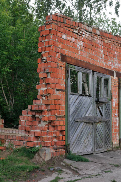 istock Broken brick wall background in sunny summer day. Abstract red brick old wall texture background. Ruins uneven crumbling red brick wall. Old gates in the wall 1162645050