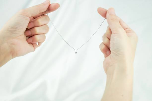 W dłoniach trzyma delikatny naszyjnik z małą zawieszką, podkreślający zimowy wybór biżuterii.