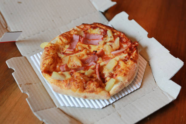 istock Hawaiian pizza in paper tray on wooden table. 1162676015