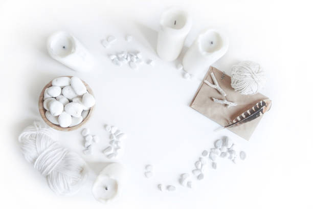 Boho white mockup with candles, cotton yarn, feathers and white sea pebble on the desk. Top view flat lay. Space for your text stock photo