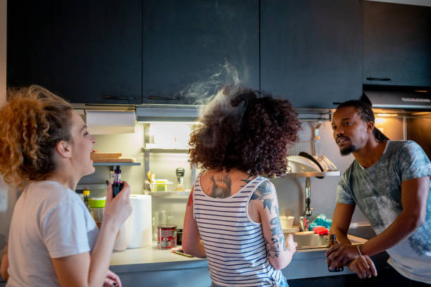 Vaping into her flatmate's hair and laughing Young woman with flatmates in the kitchen vaping into her friend's hair and laughing flatmate stock pictures, royalty-free photos & images