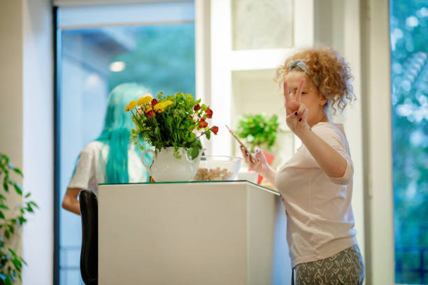 Young woman giving peace sign gesture, working with flatmate on smart phone Young woman by the kitchen bar counter with flatmate working on smart phone and showing peace sign flatmate stock pictures, royalty-free photos & images