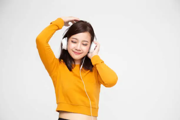 Photo of Asian woman listening music with headphones in playlist song application on smartphone, Hipster young girl concept