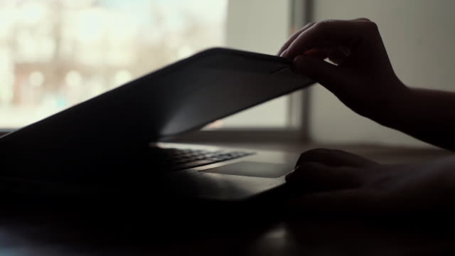 Woman hands opens the lid of a laptop close-up near the window in slow motion