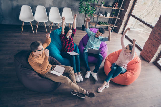 istock Above high angle view of nice attractive cheerful glad confident guys development manager employees sitting on bag chairs rising hands up attainment at industrial loft interior workplace workstation 1162711505