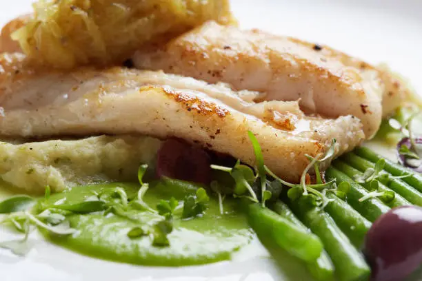 Part of a restaurant dish of grilled fish with green beans, olives and a green sauce.
