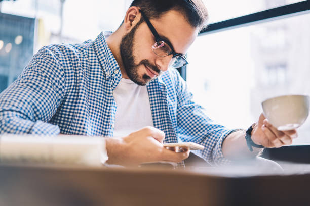 istock Pensive hipster guy concentrated making transaction via application on mobile sitting in cafe,young male blogger uploading content sharing with followers in networks via smartphone drinking coffee 1162712991