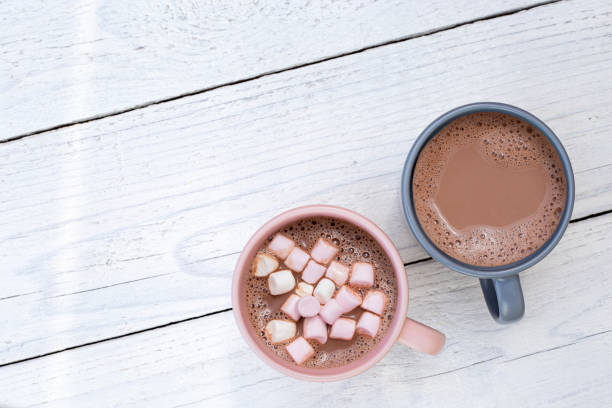 istock Hot chocolate in two mugs, one with small marshmallows, isolated on white painted wood from above. Space for text. 1162715798