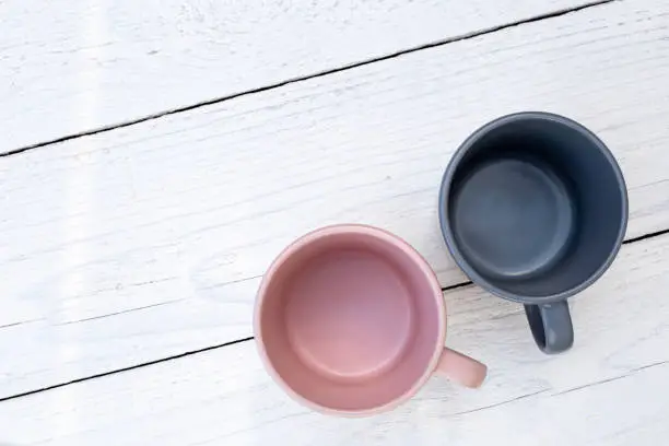 Two empty ceramic mugs, pink and blue-grey, isolated on white painted wood from above. Space for text.