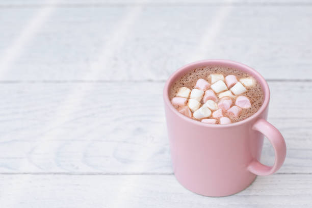 istock Hot chocolate with small pink and white marshmallows in a pink ceramic mug isolated on white painted wood. Space for text. 1162716005