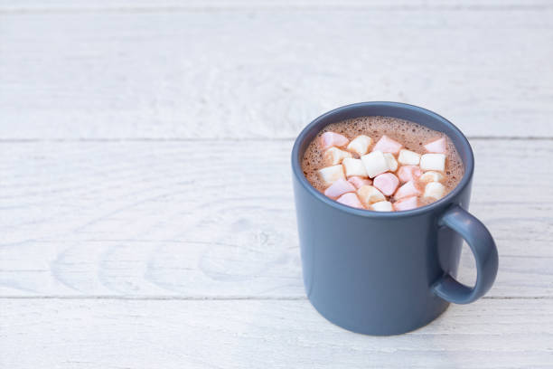 istock Hot chocolate with small pink and white marshmallows in a blue-grey ceramic mug isolated on white painted wood. Space for text. 1162716135