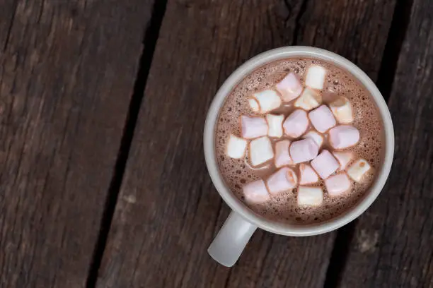 Hot chocolate with small marshmallows in a grey ceramic mug isolated on dark brown wood from above. Space for text.