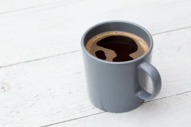 Black coffee in a blue-grey ceramic mug isolated on white painted wood. Space for text.