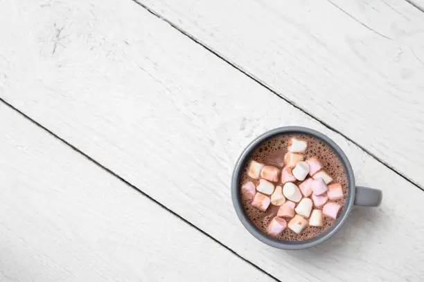 Hot chocolate with small marshmallows in a blue-grey ceramic mug isolated on white painted wood from above. Space for text.