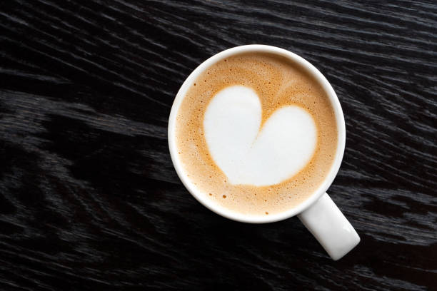 istock Cappuccino with heart shape foam in a white ceraamic mug isolated on dark brown wood table with grain from above. Space for text. 1162716611