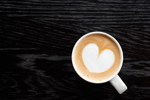 istock Cappuccino with heart shape foam in a white ceraamic mug isolated on dark brown wood table with grain from above. Space for text. 1162716639