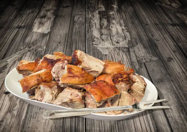 Photograph of gourmet freshly spit roasted pork shoulder chunks, offered on old, weathered, cracked, flaky, rustic wooden backdrop.