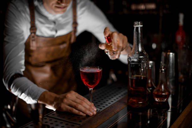 Professional bartender spraying on the red alcoholic cocktail in the dark