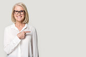 Happy old woman in glasses showing to copyspace blank space