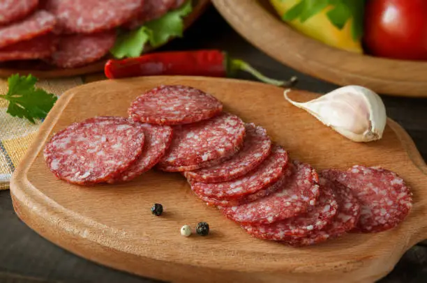 Slices of salami with vegetables pepper and garlic on a cutting board on a wooden table.