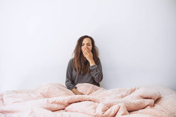 The girl is in bed and yawns The girl is in bed and yawns. She covers her mouth with her hand. Early morning and she is sleepy. waking up stock pictures, royalty-free photos & images