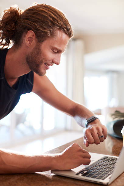istock Millennial white man checking fitness app on smartwatch using laptop after a workout, side view 1162733086