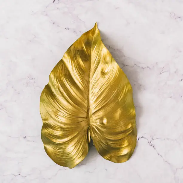 Photo of Creative layout made of golden tropical leaf on white marble texture background.