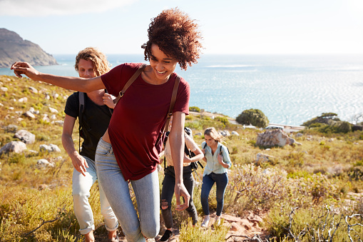 Mother and three teenage kids are hiking in Sicily, Italy. They are hiking on the hill near the town of Cefalu. Family is walking on a difficult path on a steep  side of the hill. Sunny spring day.\nCanon R5