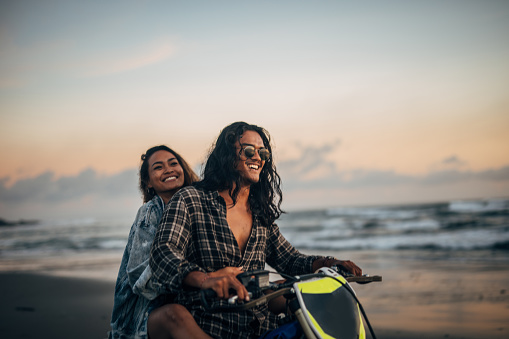 Man and woman, young couple on the beach, riding on a motorcycle together.