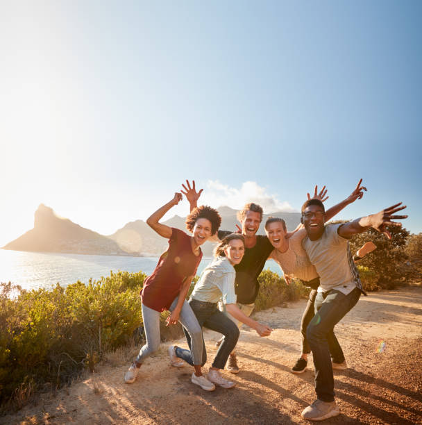 Five millennial friends on a road trip have fun posing for photos on a coastal path, full length Five millennial friends on a road trip have fun posing for photos on a coastal path, full length cheering photos stock pictures, royalty-free photos & images