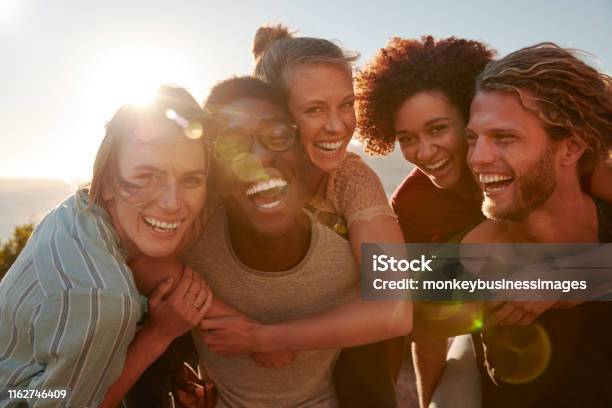 Five Millennial Friends On A Road Trip Have Fun Piggybacking At The Roadside Front View Lens Flare Stock Photo - Download Image Now
