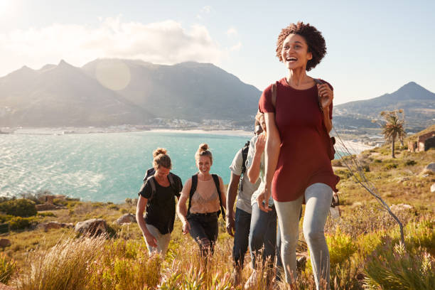 millennial african american woman leading friends on an uphill hike by the coast, close up - people traveling journey group of people hiking imagens e fotografias de stock