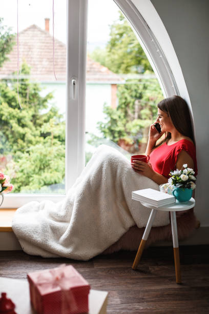 istock Woman talking on cell phone while relaxing by the window 1162753921