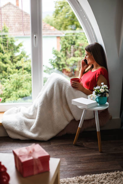 istock Woman talking on cell phone while relaxing by the window 1162753922