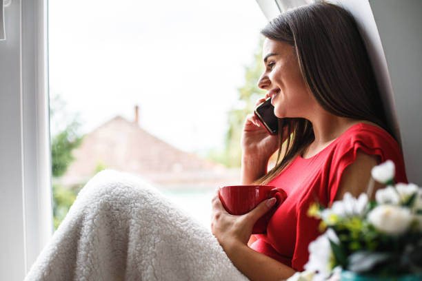 istock Happy woman having tea and talking on cell phone while relaxing at home 1162753926