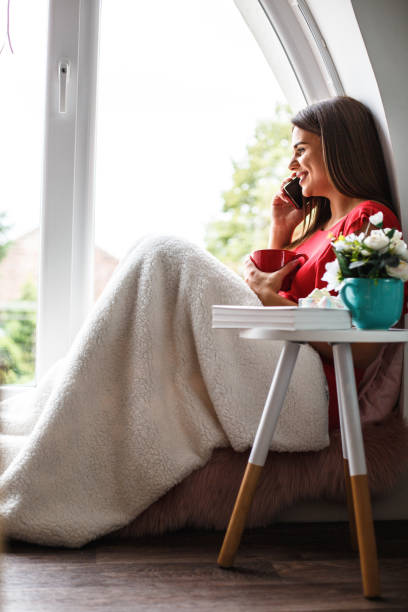 istock Happy woman having tea and talking on cell phone while relaxing at home 1162753934