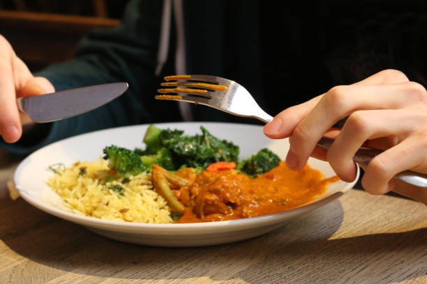 image de manger dehors avec la nourriture indienne faite maison de restaurant de poulet tikka masala le repas, le riz pilau aromatisé au safran jaune, les légumes verts et le brocoli sur la table en bois de salle à manger, l'homme mangeant le déjeuner  - delhi equipment household equipment decor photos et images de collection