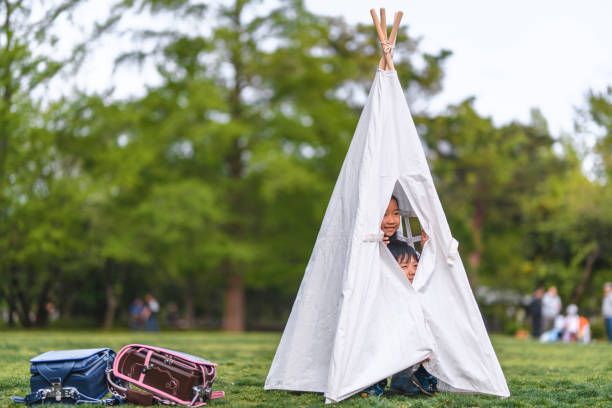 Elementary age Japanese schoolchildren putting aside their randoseru to play in teepee at public park.