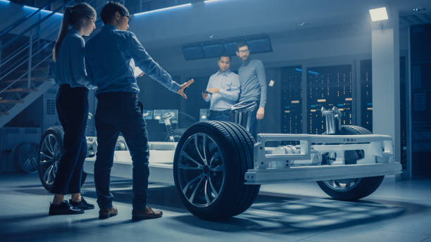 istock Team of Automotive Engineers Discussing and Designing Electric Car Platform Chassis Prototype, Taking Measures, Working with 3D CAD Software, Checking Quality Control. Vehicle Frame with Wheels, Engine and Battery. 1162762001