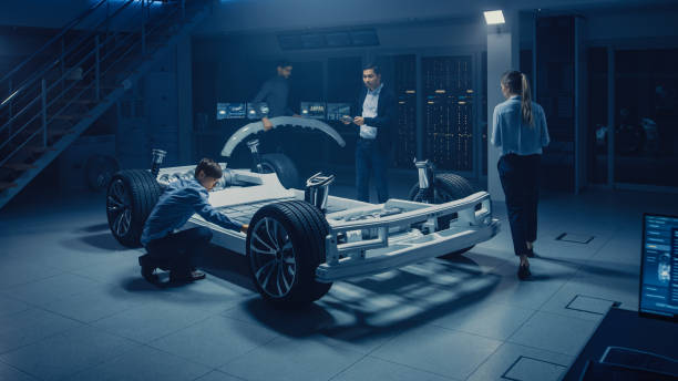 istock Team of Automotive Engineers Working on Electric Car Platform Chassis, Taking Measures, working with 3D CAD Software, Analysing Efficiency. Vehicle Frame with Wheels, Engine and Battery. 1162762179